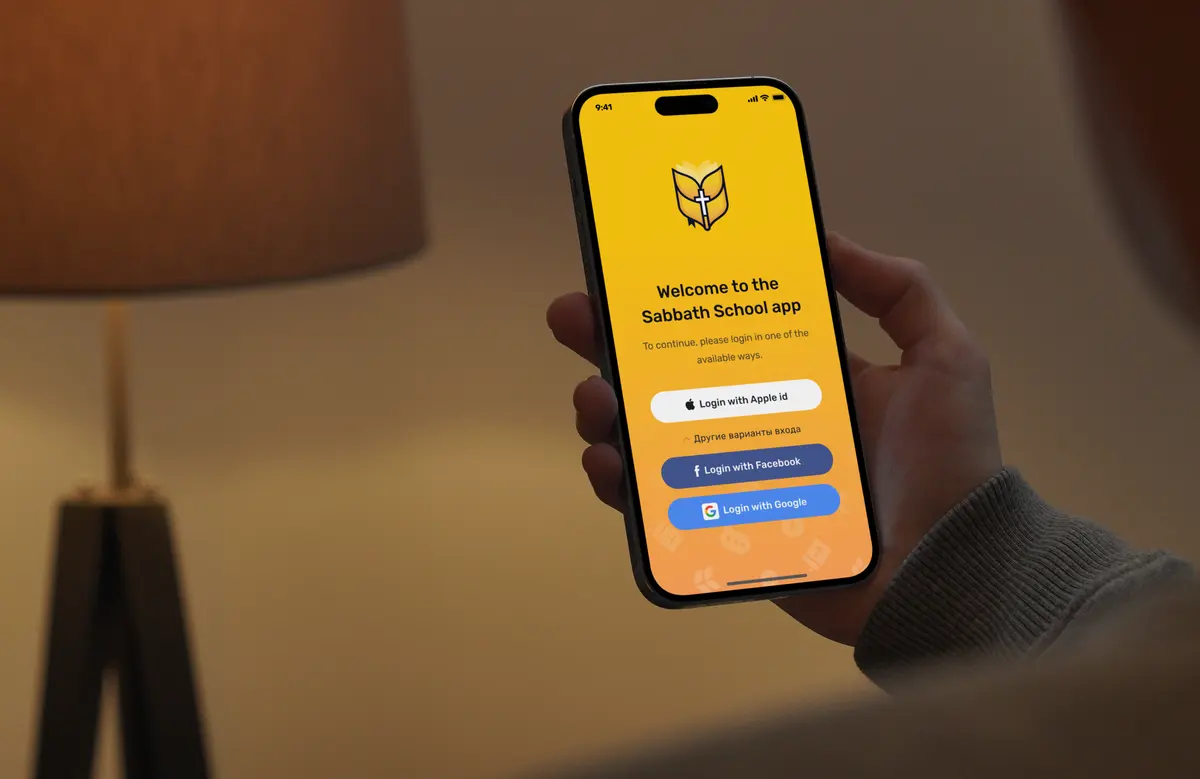 A phone held in a warm room showing the Sabbath School app welcome screen