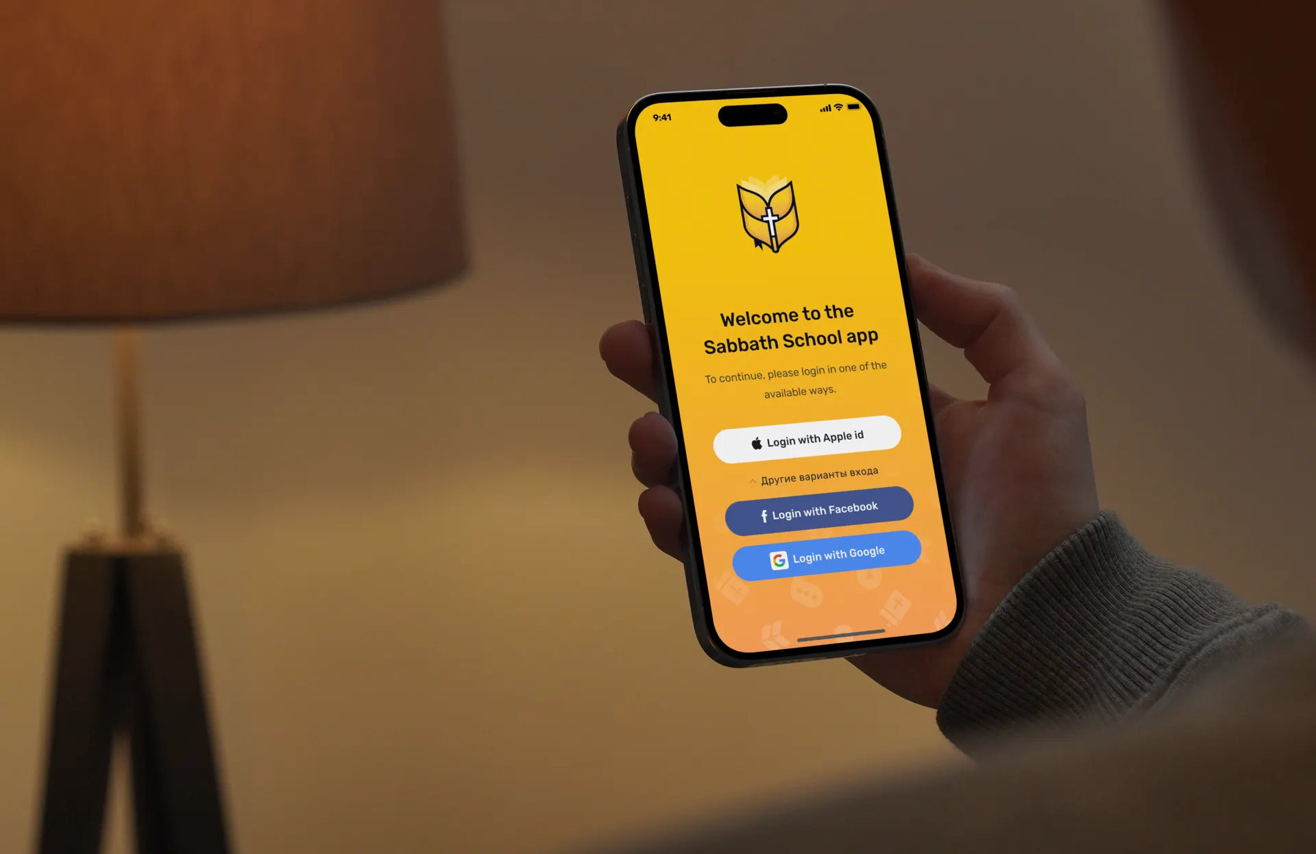 A phone held in a warm room showing the Sabbath School app welcome screen